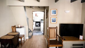 Un salon avec une table à manger en bois, deux chaises, un téléviseur et une cuisine visible à travers une porte ouverte.