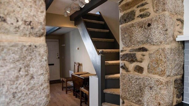 Un escalier avec un mur en pierre d’un côté et un plancher en bois menant à un coin repas équipé de chaises et d’une table.