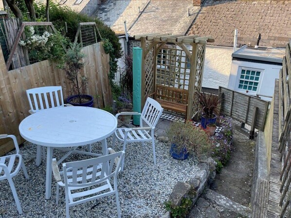 A patio with a round table and four chairs, surrounded by a wooden fence and potted plants.