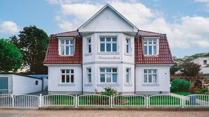 Ein zweistöckiges Haus mit weißer Fassade und rotem Dach, ausgestattet mit einem Hauseingang und einer Namensschild.