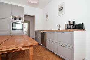 Cozinha moderna com armários cinza, mesa de madeira e cafeteira.