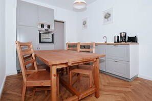 A modern kitchen with white cabinetry, a wooden dining table, and a coffee maker. - Modern vacation rental in Ahlbeck, just 400 meters from the beach (Seebad Ahlbeck)