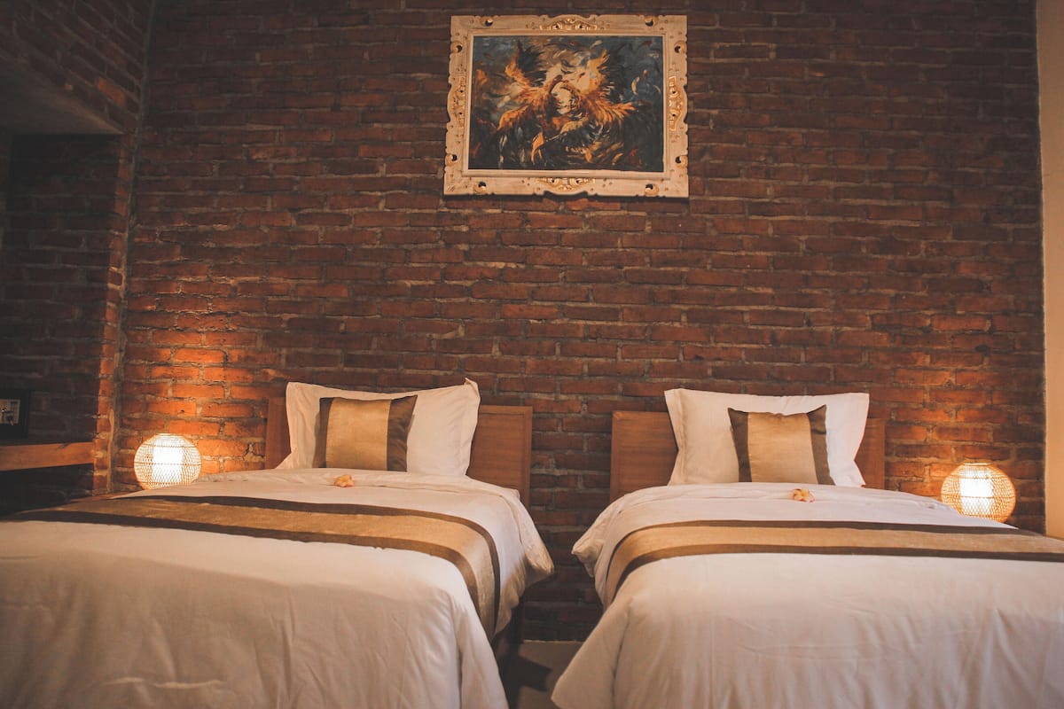 A hotel room with two beds, a brick wall, and a framed painting above the beds.