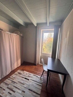 Une pièce avec un plancher en bois, une table, une fenêtre avec des rideaux et un radiateur.