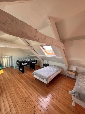 Une chambre située dans un espace de type « loft », avec un plancher en bois, un lit, un futon, une table de baby-foot et une lucarne.