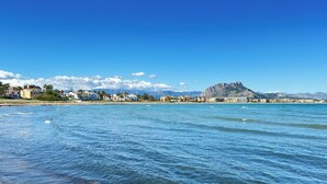Une vue sur la côte, avec une eau d’un bleu limpide, une montagne lointaine et des bâtiments qui bordent le rivage.