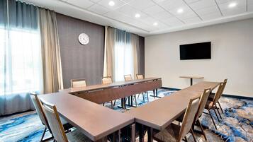 A conference room with a long table and chairs, a clock on the wall, and a flat-screen TV.