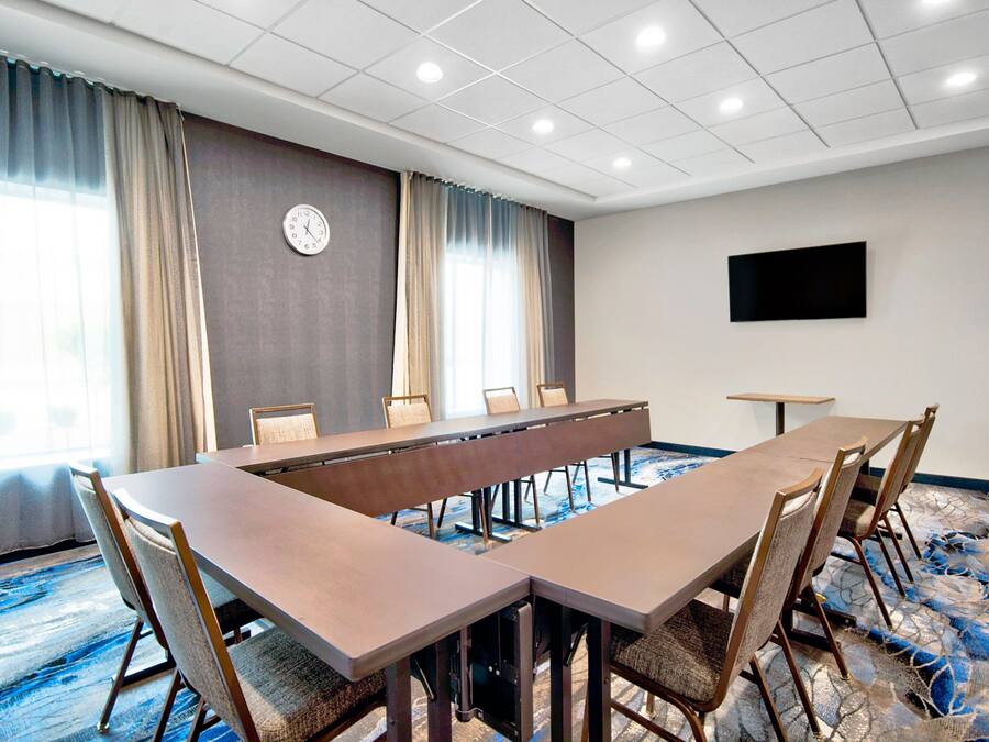A conference room with a long table and chairs, a clock on the wall, and a flat-screen TV.