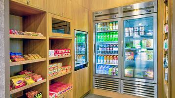 Een plek met snacks en drankjes, met houten planken vol chips en een koelgedeelte met diverse dranken en lekkernijen.