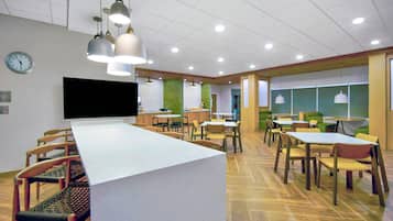 Un espace repas moderne avec une longue table, des chaises, des luminaires suspendus et une horloge au mur.