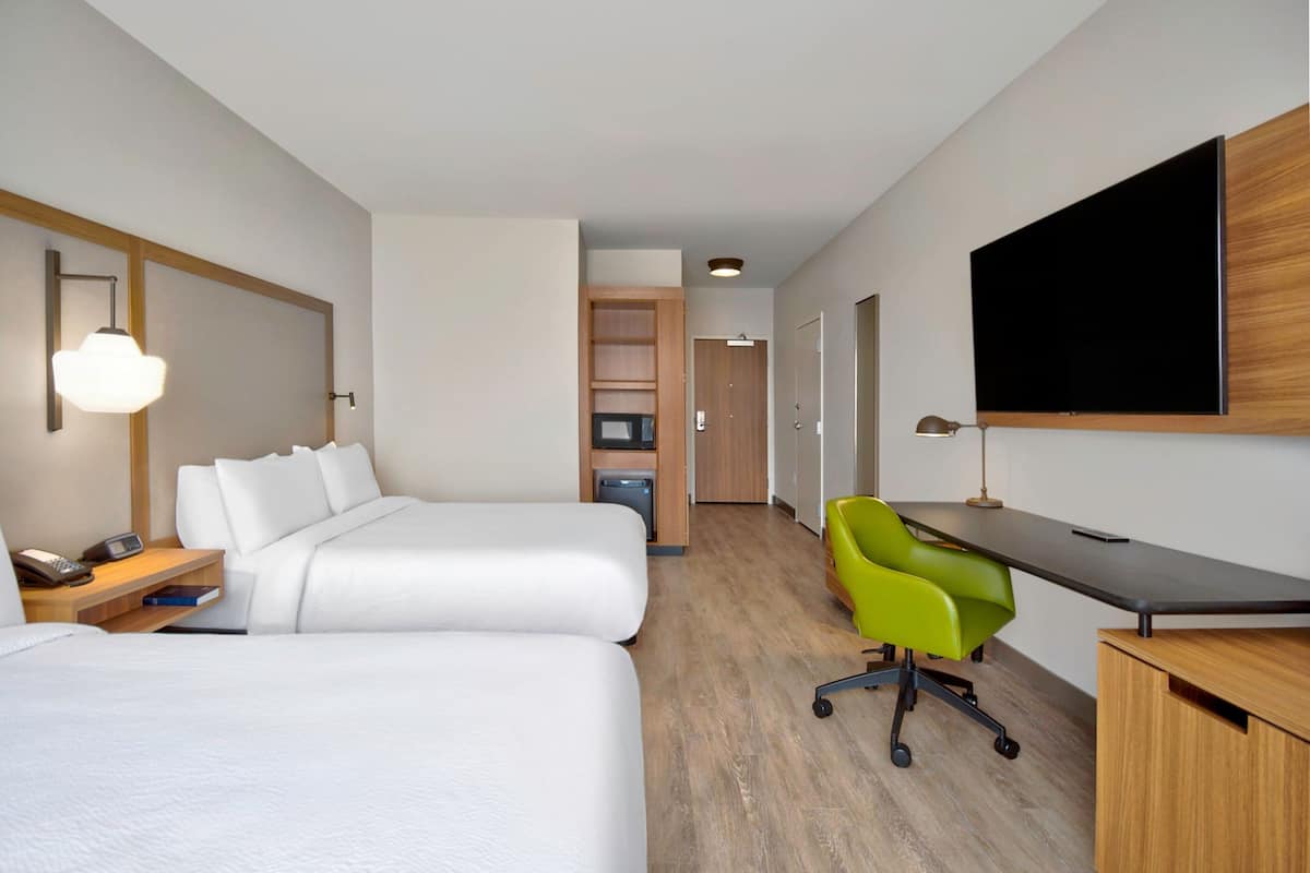 A hotel room with two beds, a desk, a TV, and a bright green chair.