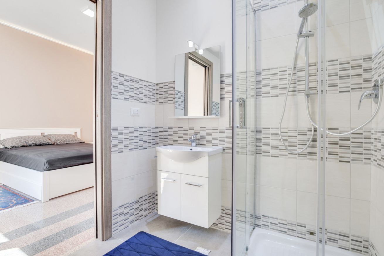 Un bagno moderno con cabina doccia in vetro, un lavandino bianco e uno specchio sopra.