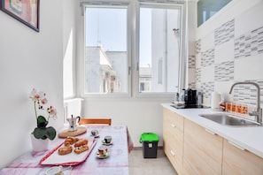 A small kitchen with a window, a sink, a coffee maker, and a trash bin.