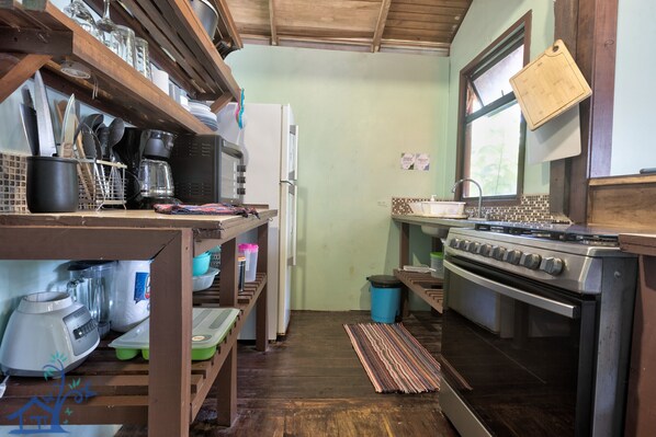 A compact kitchen with a refrigerator, stove, and wooden shelves.