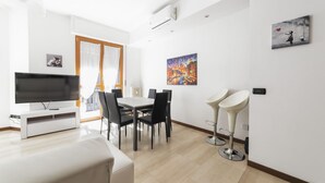 A modern living room with a flat-screen TV, dining table, chairs, and a white sofa.