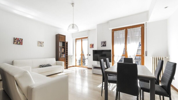 A modern living room with a white sofa, a dining table with chairs, a TV, and a bookshelf.