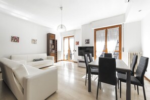 A modern living room with a white sofa, a dining table with chairs, a TV, and a bookshelf. - GuestHost - Cenisio M5 Beautiful apartment with a balcony! (Milano)