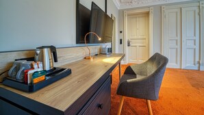 Ein Hotelzimmer mit Schreibtisch aus Holz, einem Sessel, einem Flachbildfernseher, einer Kaffeemaschine und einem Tablett mit Tassen und einem Teebeutel.