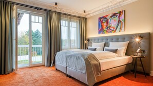 Ein Schlafzimmer mit einem großen Bett, Blick durch eine Glastür und einem farbenfrohen Gemälde an der Wand.