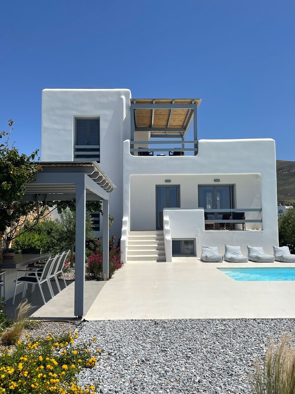 A modern white villa with a pool, outdoor seating, and a covered patio area.