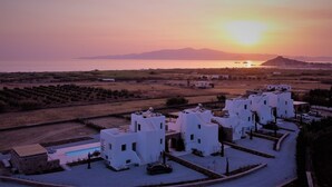 Une station balnéaire avec des bâtiments blancs, une piscine et une vue sur le coucher de soleil sur la mer.