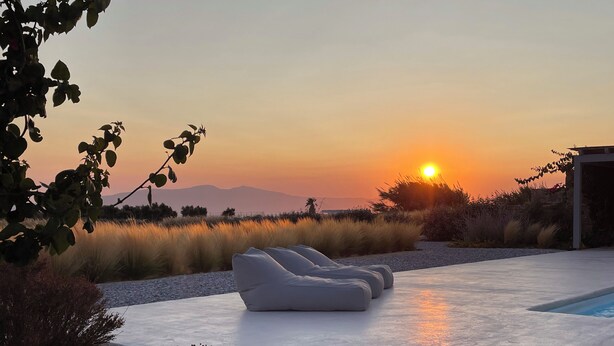 Un espace de détente extérieur moderne, doté d’une piscine, entouré de verdure et offrant une vue imprenable sur le coucher de soleil.
