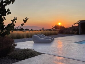 Un espace de détente extérieur moderne, doté d’une piscine, entouré de verdure et offrant une vue imprenable sur le coucher de soleil.
