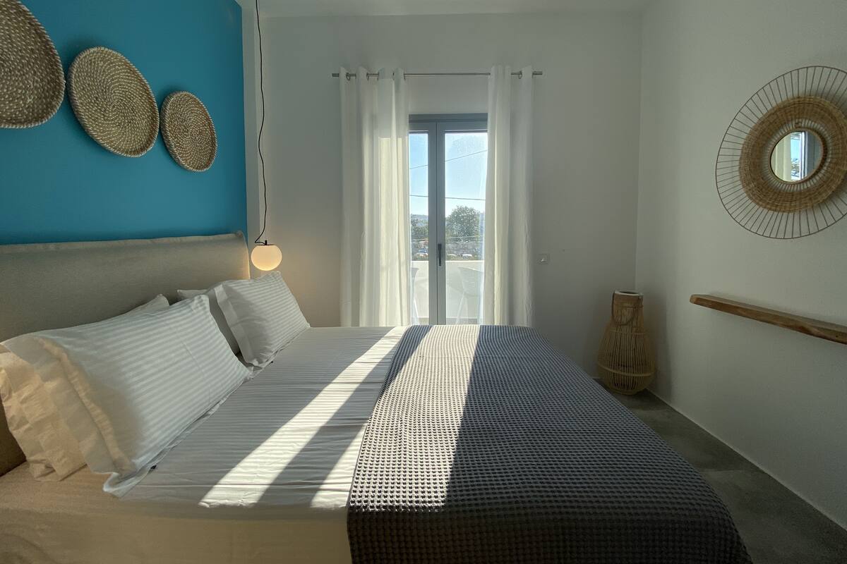 A bedroom with a bed, a hanging light, a window with curtains, and a view of the outside.