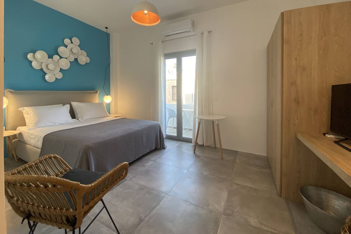 A bedroom with a bed, a chair, a TV, and a balcony.