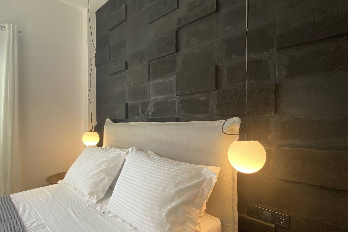 A modern bedroom with a headboard, a bed with white bedding, and two bedside lamps.