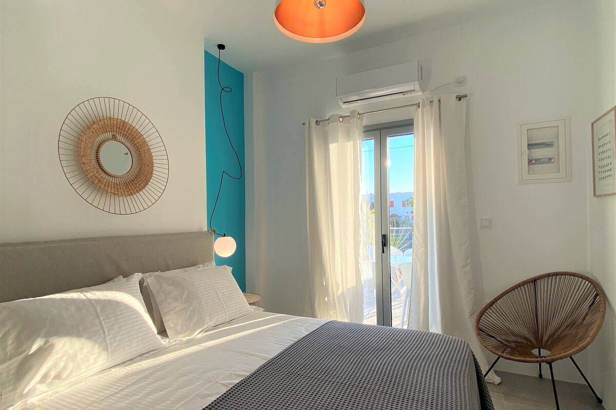A bedroom with a bed, a hanging light fixture, a chair, and a window with curtains.