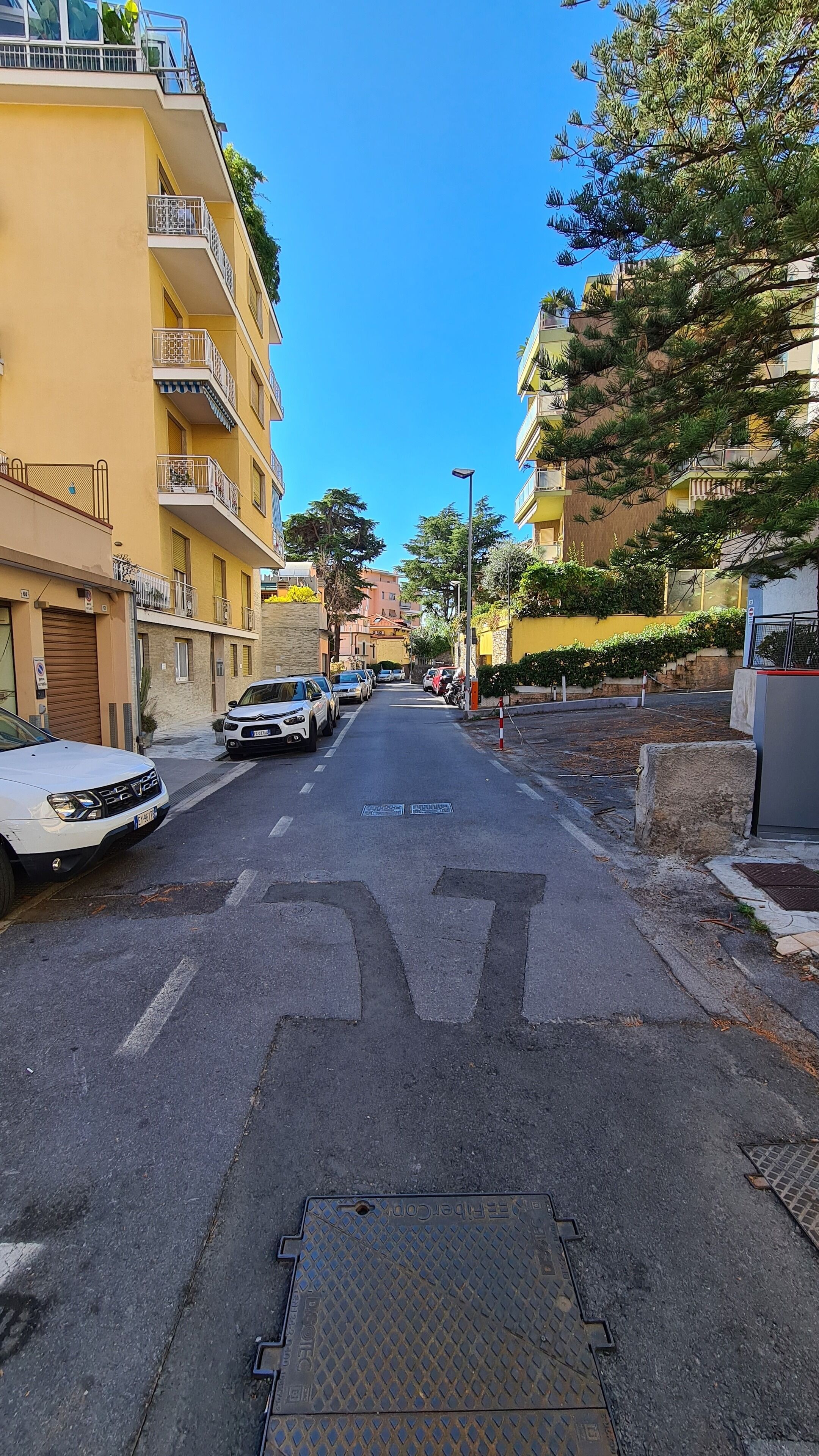 Una calle con coches estacionados, edificios amarillos y un cielo azul despejado.