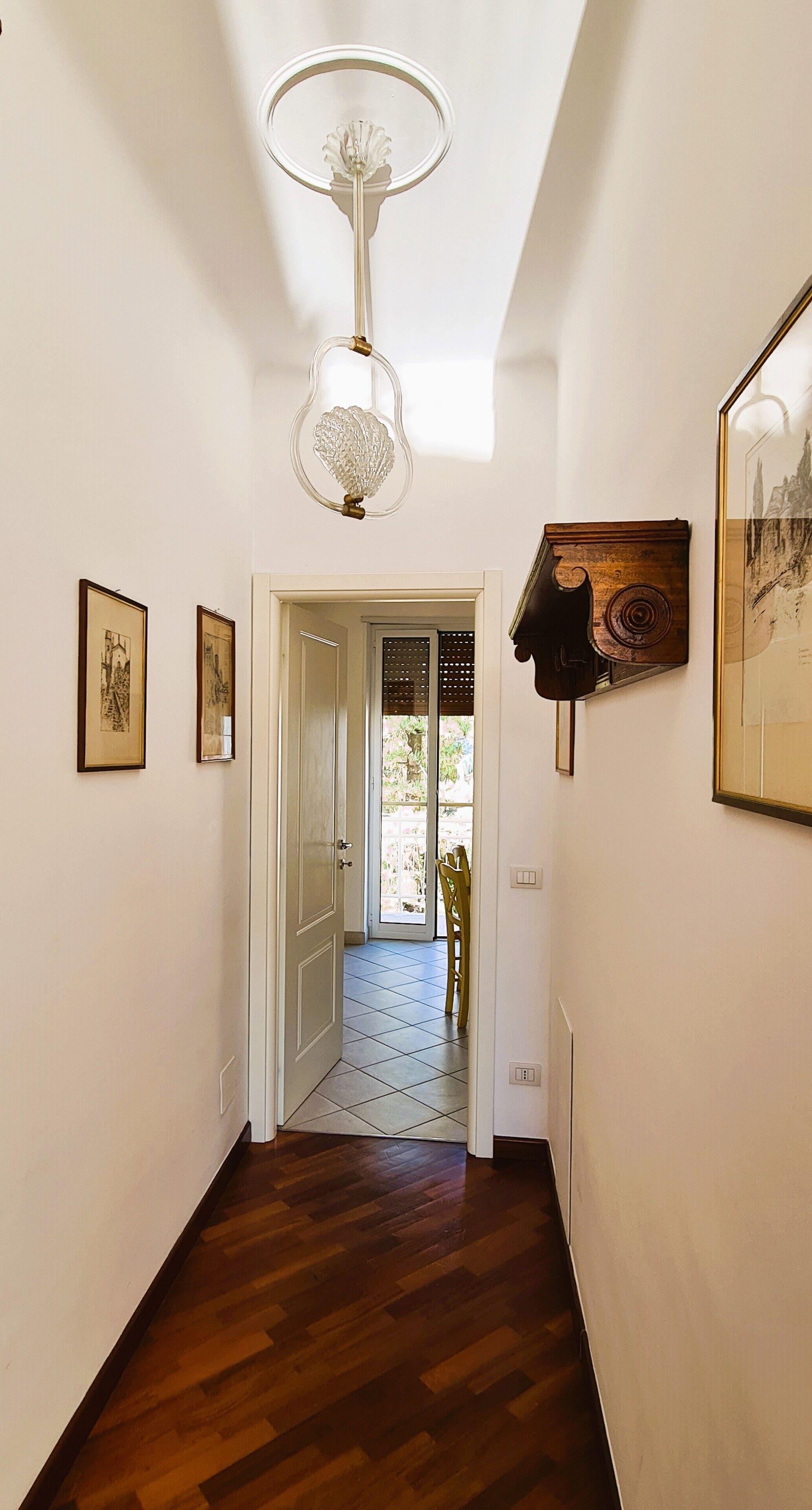 A hallway with wooden flooring, a white door at the end, and framed pictures on the walls.