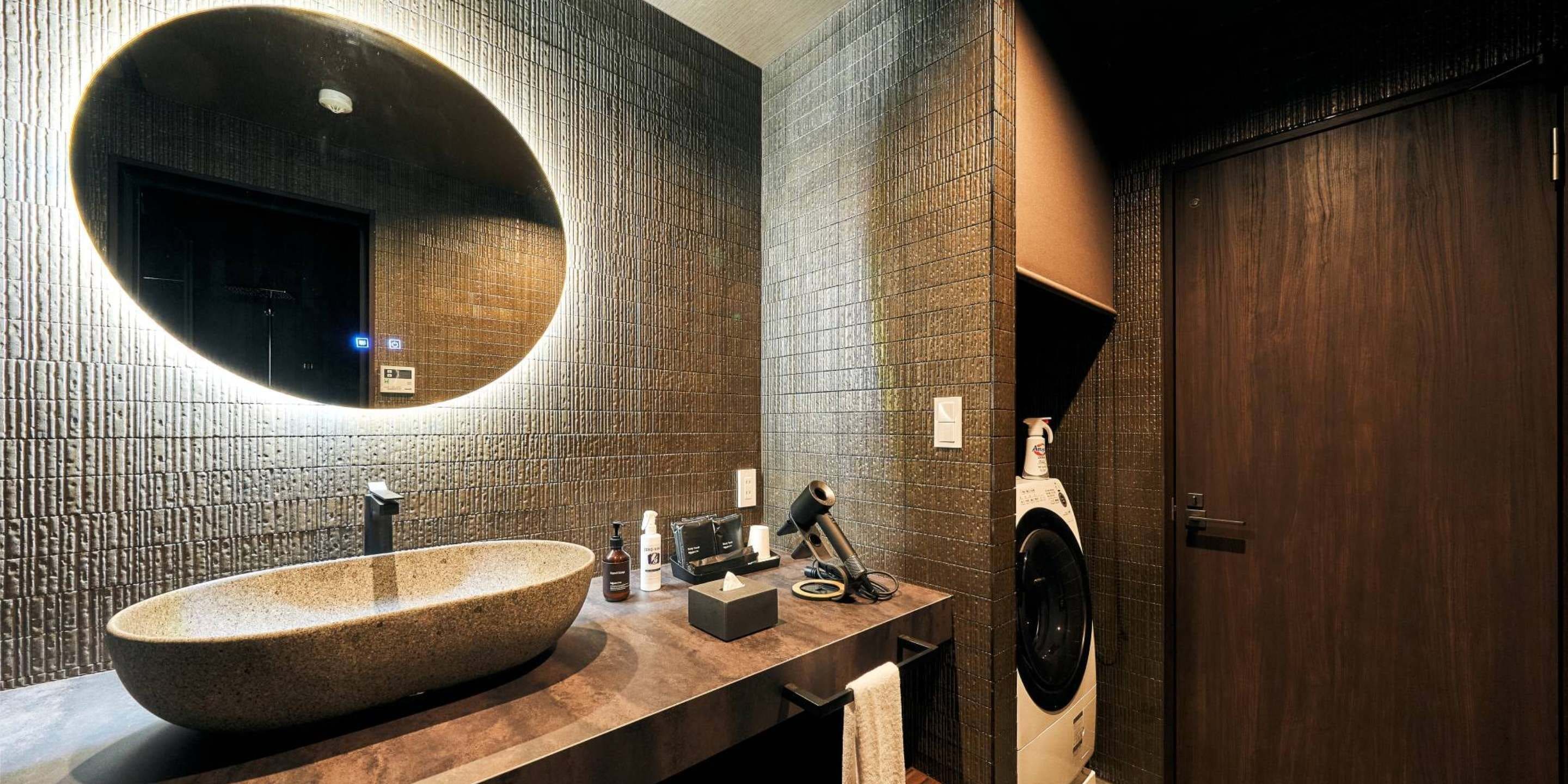 A modern bathroom with a large freestanding sink, a round mirror, and a built-in washing machine.