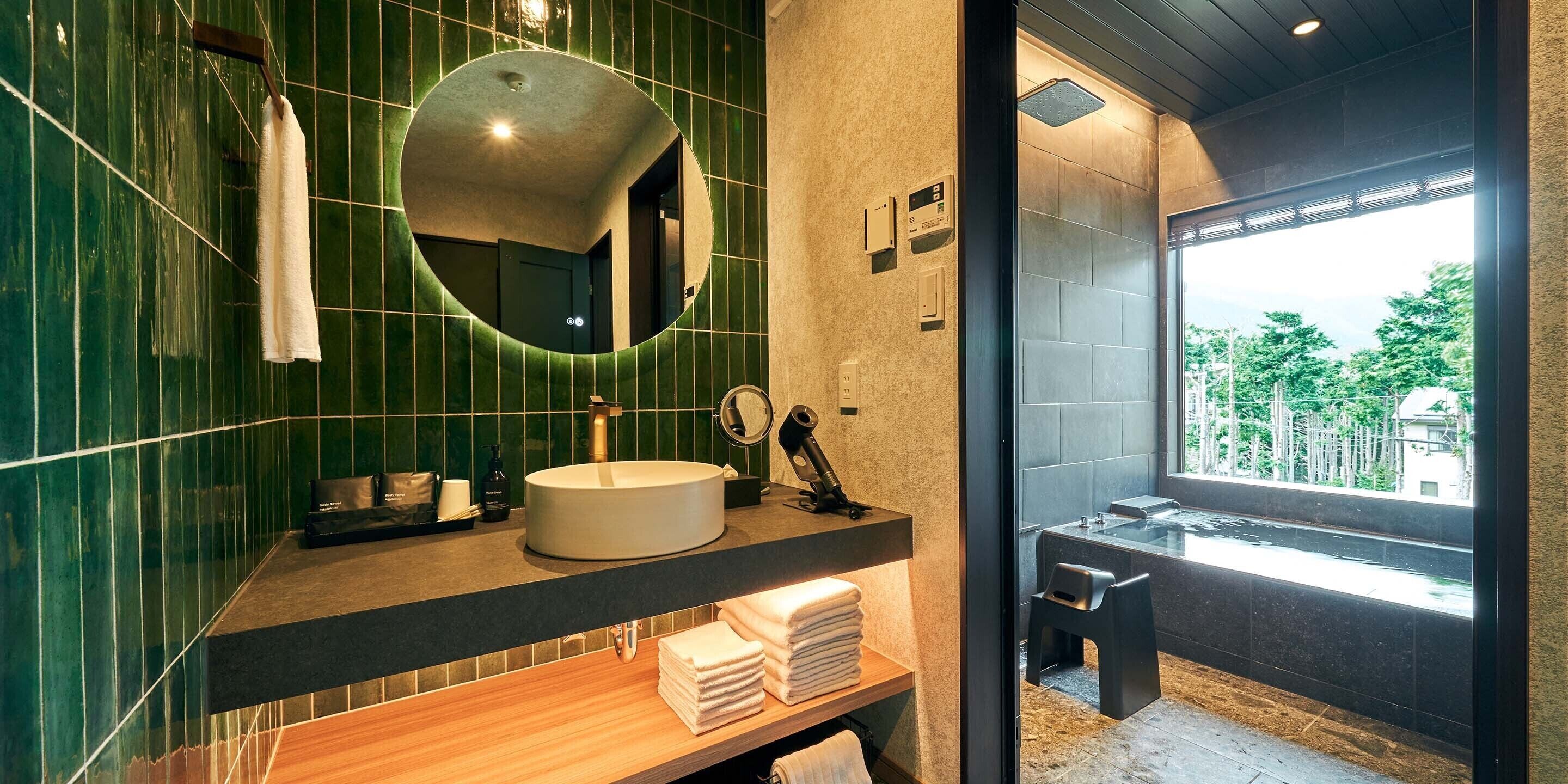 Een moderne badkamer met een ronde spiegel, een wastafel en uitzicht op buiten.