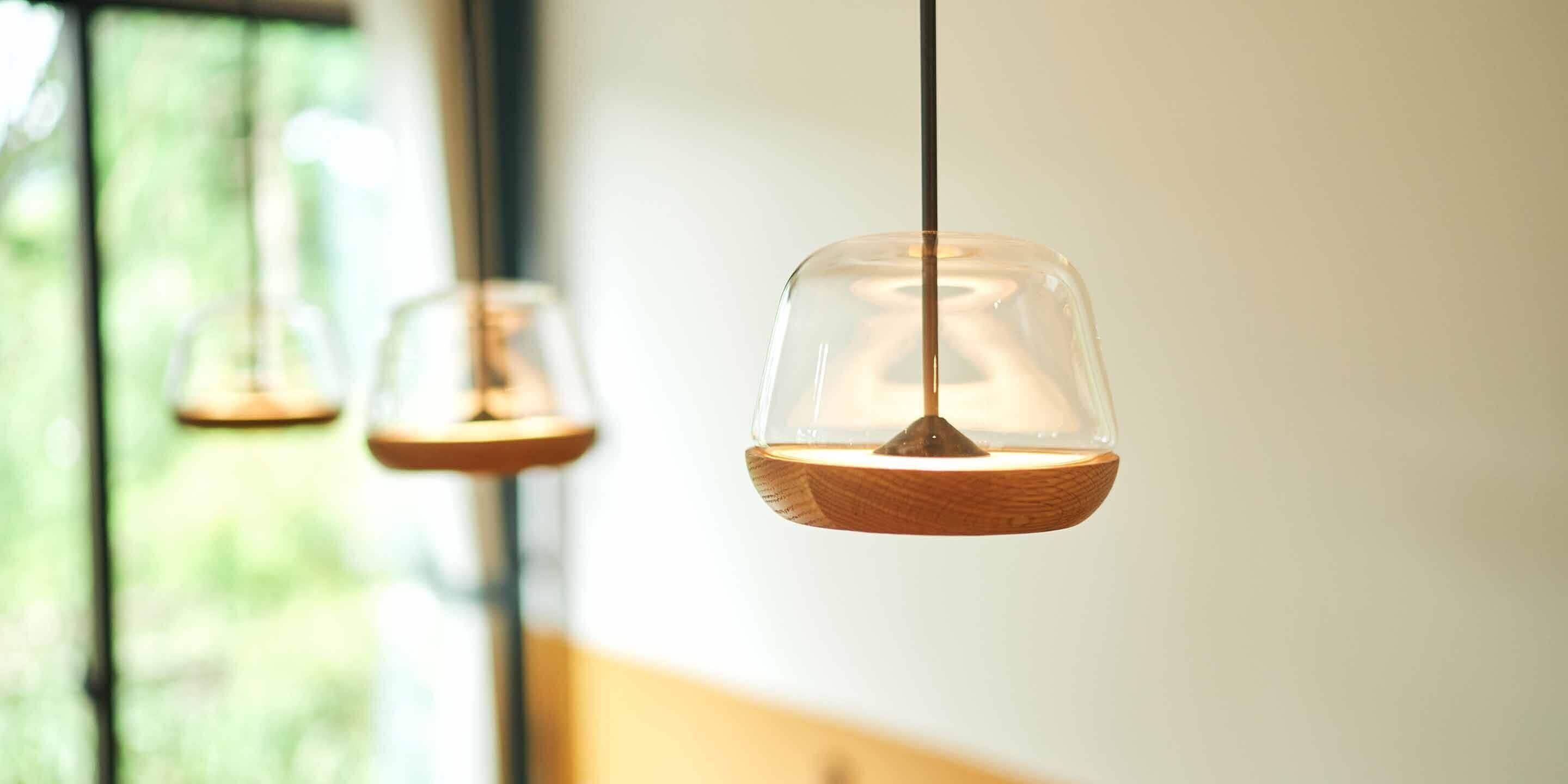 Un luminaire suspendu composé d’un abat-jour en verre transparent et d’une base en bois, fixé au plafond.