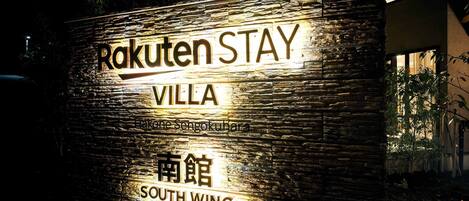 Ein Schild für Rakuten Stay Villa mit Steinverkleidung und beleuchteter Schrift.