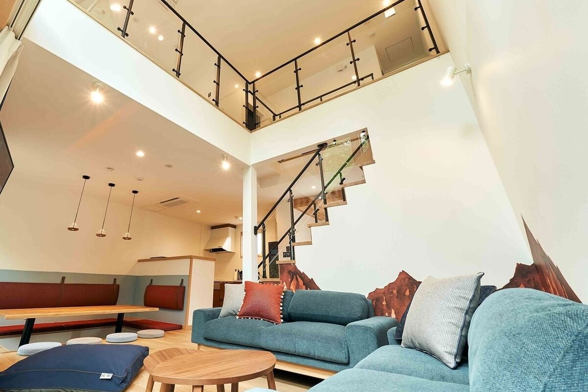 Amplia sala de estar con sofá azul, mesa de centro de madera y una escalera que lleva a un nivel superior.