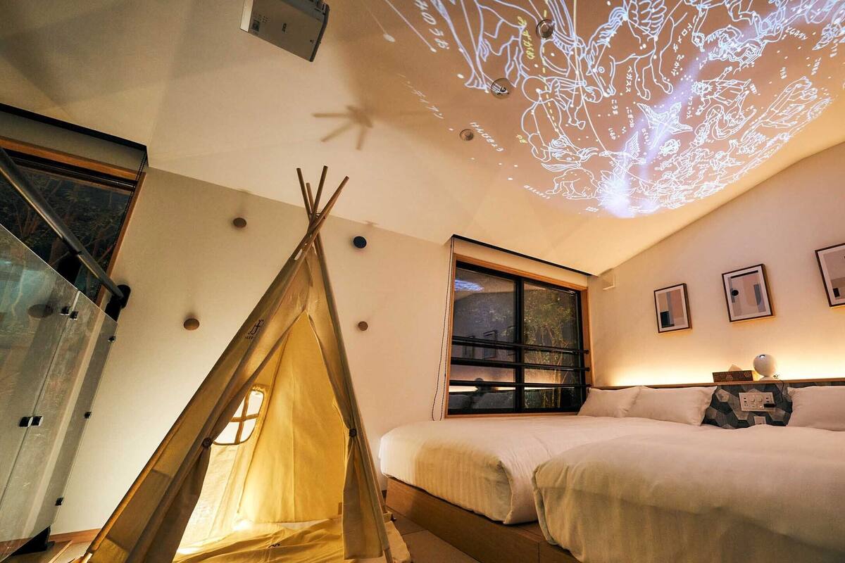 Una habitación acogedora con una cama, una ventana, un proyector mostrando un árbol y una tienda de campaña.