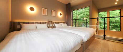 A modern hotel room with a large bed, a view of trees through a balcony, and wall-mounted lighting.