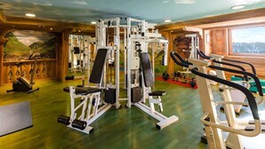 Ett gym med olika typer av träningsutrustning, inklusive styrketräningsmaskiner och konditionsmaskiner, i ett rum med träväggar och en väggmålning som föreställer ett landskap.