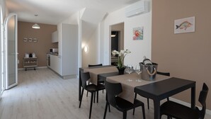 Moderni ruokailutila, jossa on neljälle katettu ruokapöytä, taustalla keittiö ja käytävä, joka johtaa toiseen huoneeseen.