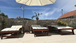 A patio with three wooden lounge chairs, a large umbrella, and a stone wall backdrop.