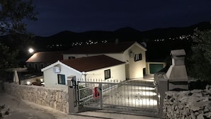 A two-story house with a stone wall and a metal gate.