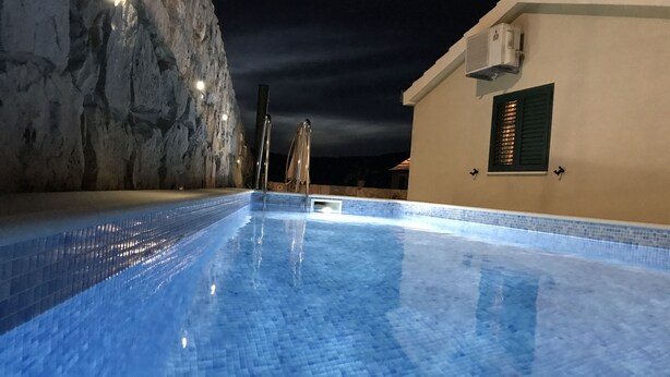 A swimming pool with clear blue water, a stone wall, and a building with a tiled roof.