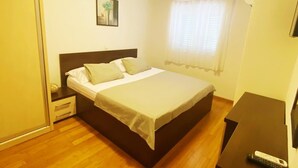 A bedroom with a bed, a nightstand, a bedside table, a painting on the wall, and a window with curtains.