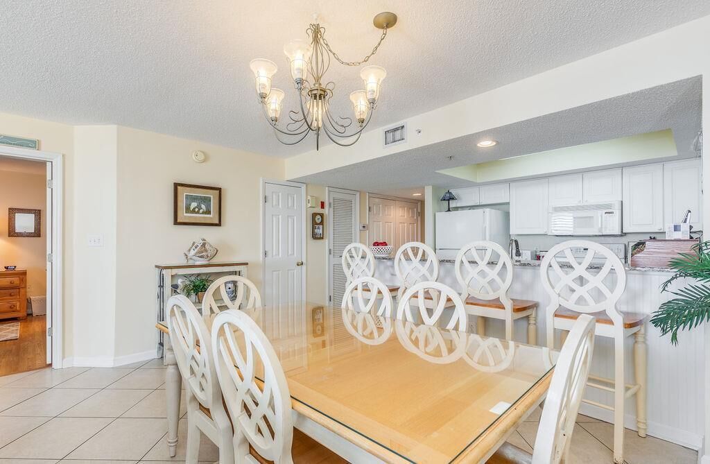 Un comedor con una mesa de madera y sillas blancas, una araña y armarios blancos al fondo.