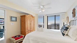 Quarto com uma cama grande, um guarda-roupa de madeira, um pequeno banco e uma varanda com vista.