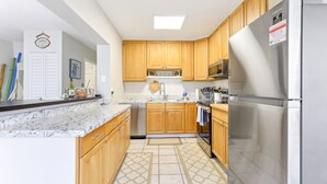 A modern kitchen with wooden cabinets, a stainless steel refrigerator, and a marble countertop. - Jensen Beach Home: Walk to Beach Access! (Jensen Beach)