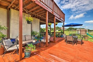 Relax on the covered patio with a sofa, dining table, and potted plants, surrounded by a grassy lawn and a playground.